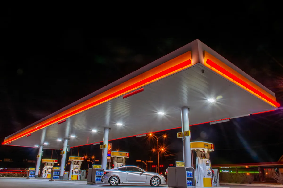 Station-service Shell éclairée la nuit, voiture garée devant les pompes automatiques