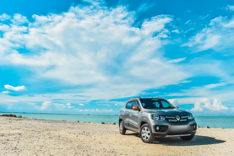 Voiture garée sur une plage ensoleillée au bord de la mer, prête pour un départ en vacances