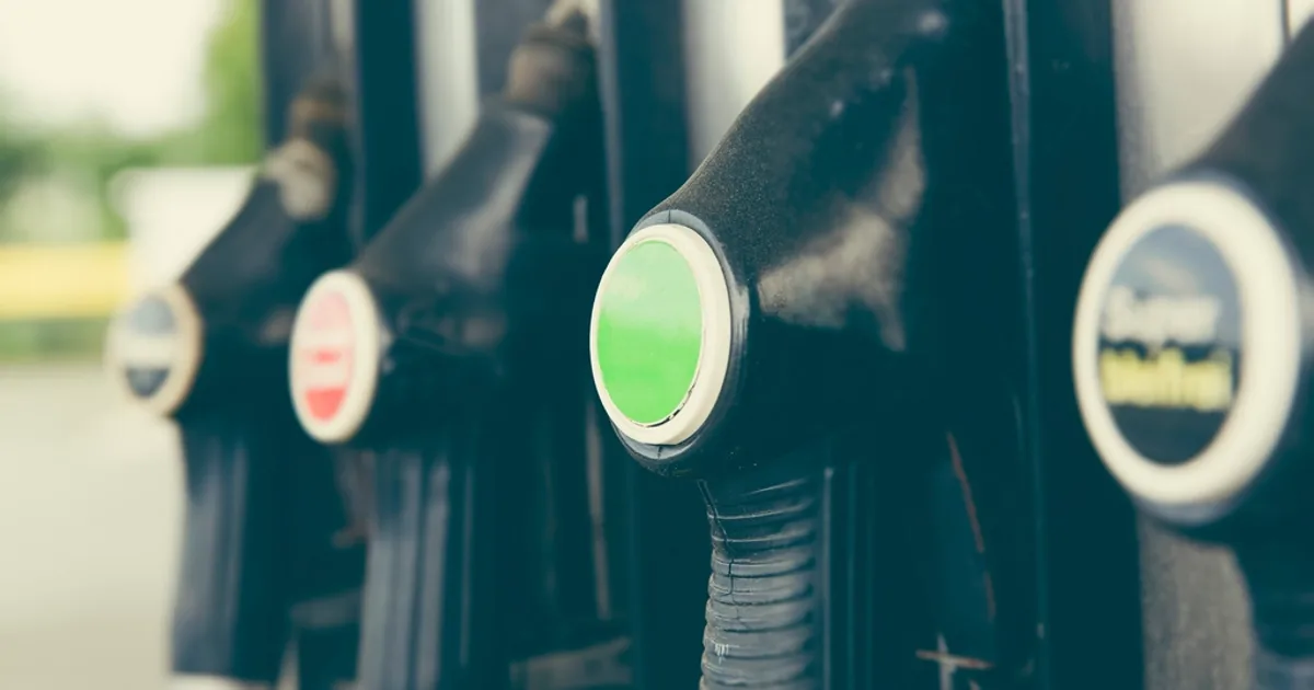 Rangée de pistolets de distribution noirs sur une pompe de station-service, repères de couleur visibles sur les embouts