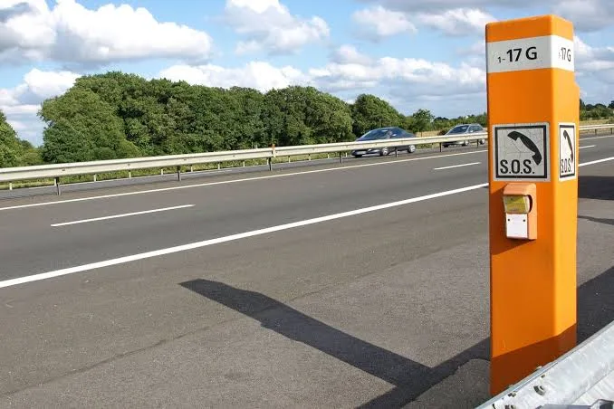 Borne d'appel d'urgence SOS orange au bord d'une autoroute, derrière la glissière de sécurité