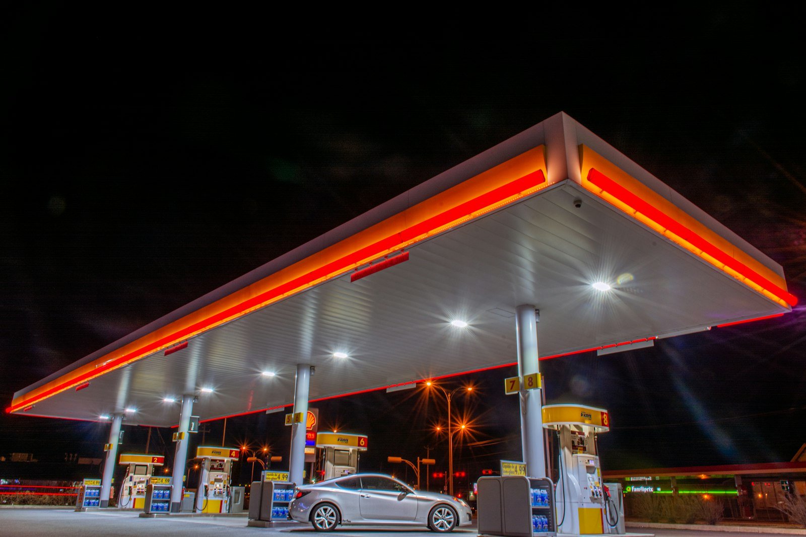 Station-service Shell éclairée la nuit, voiture garée devant les pompes automatiques